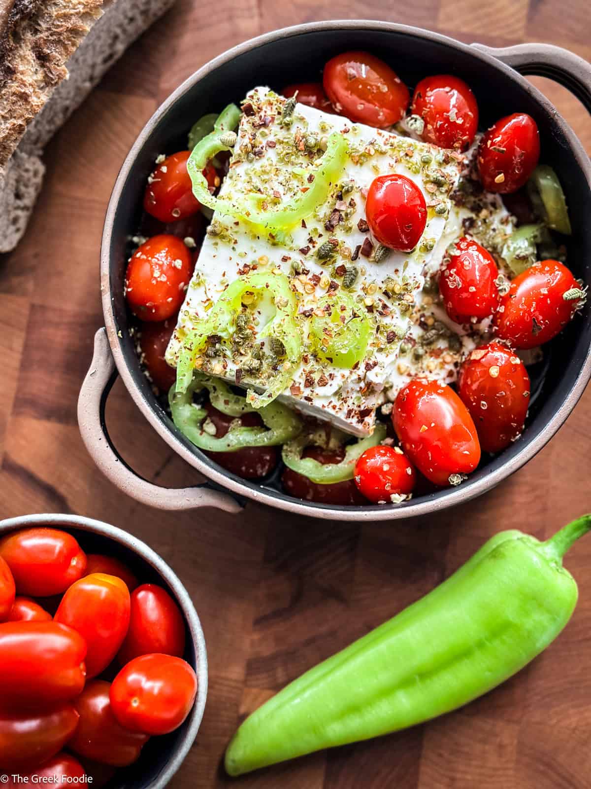 A ceramic dish with feta tomatoes and sliced peppers with a pepper and a bowl of cherry tomatoes on a table.