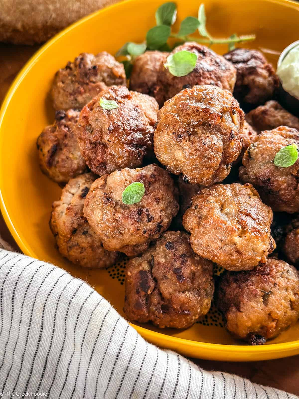 A yellow plate full of meatballs on a table, and a cloth napkin.