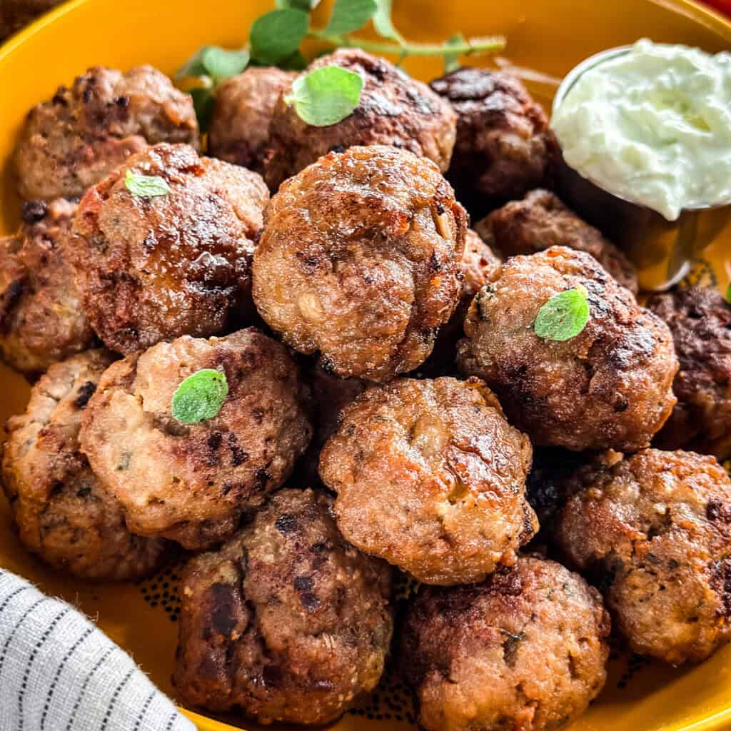 A yellow plate full of meatballs on a table, and a cloth napkin.