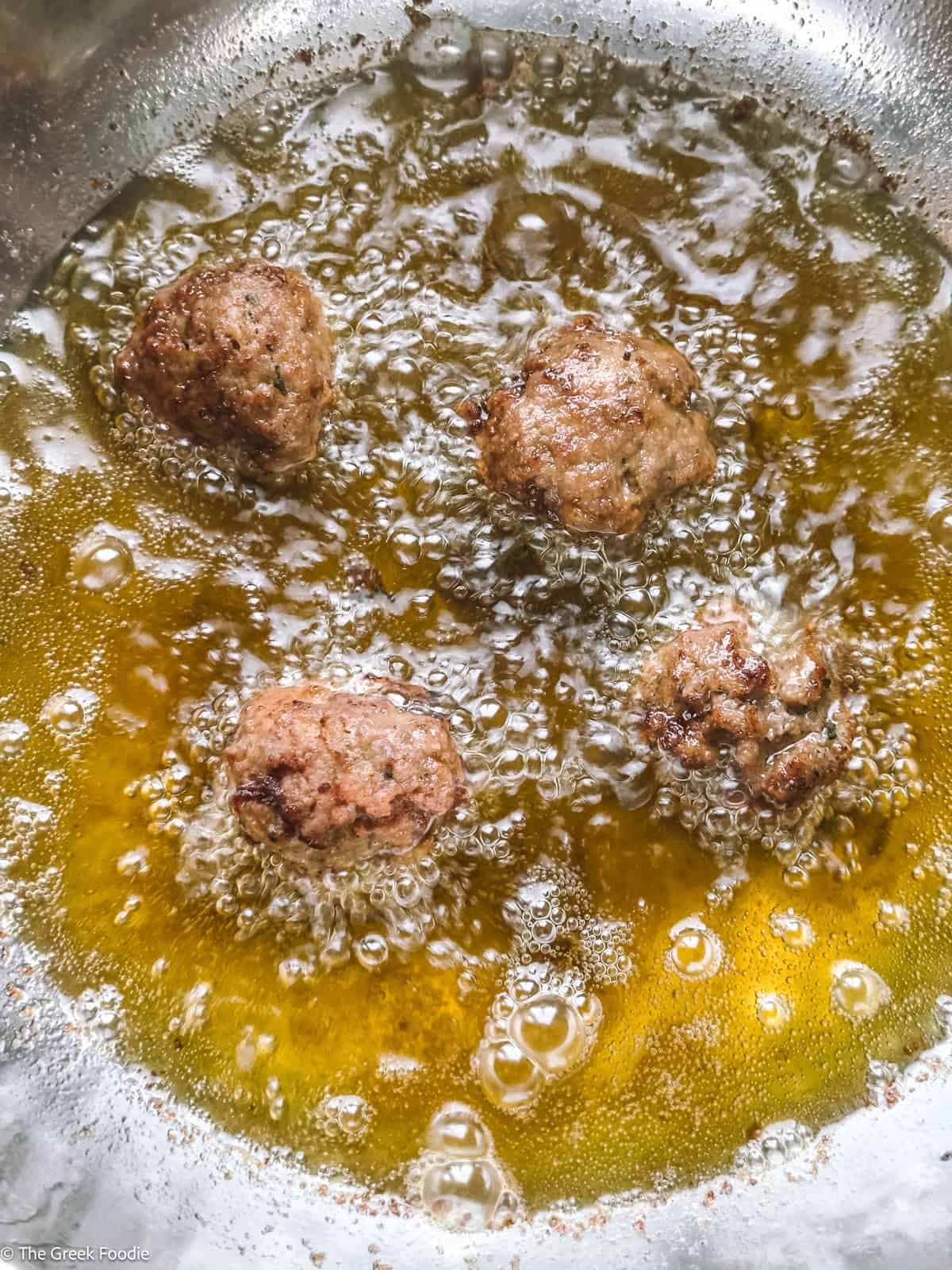 Four meatballs frying in oil.
