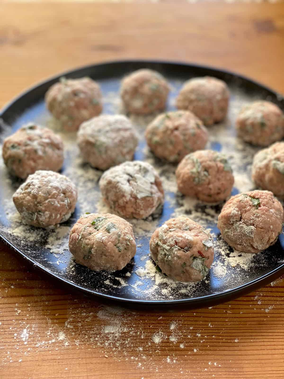 Formed meatballs dusted with flour on a plate.
