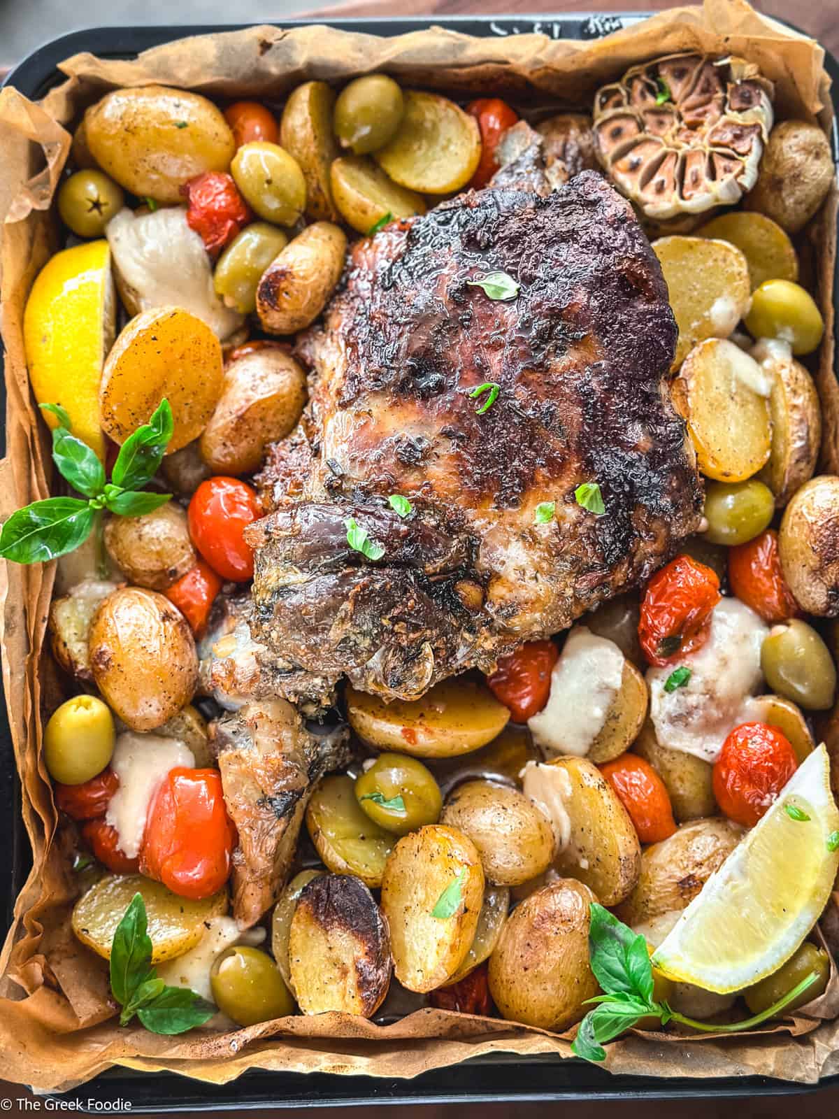 A leg of lamb with potatoes, tomatoes, olives and herbs in parchment paper.