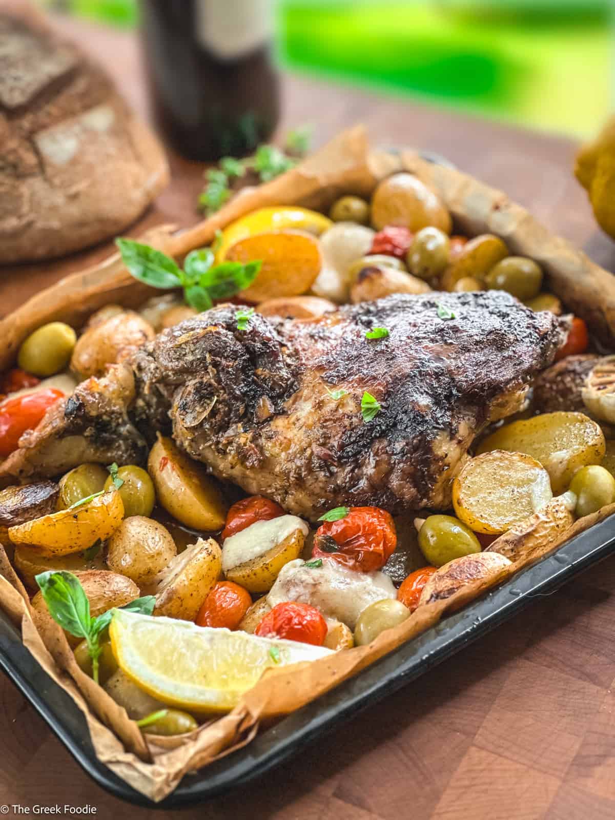 A leg of lamb with potatoes, tomatoes, olives and herbs in parchment paper.