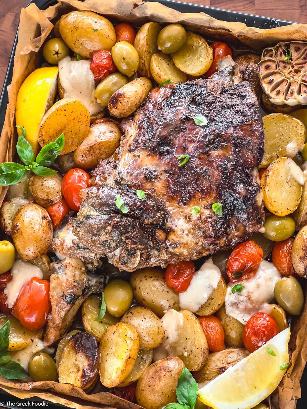 A leg of lamb with potatoes, tomatoes, olives and herbs in parchment paper. Pin.