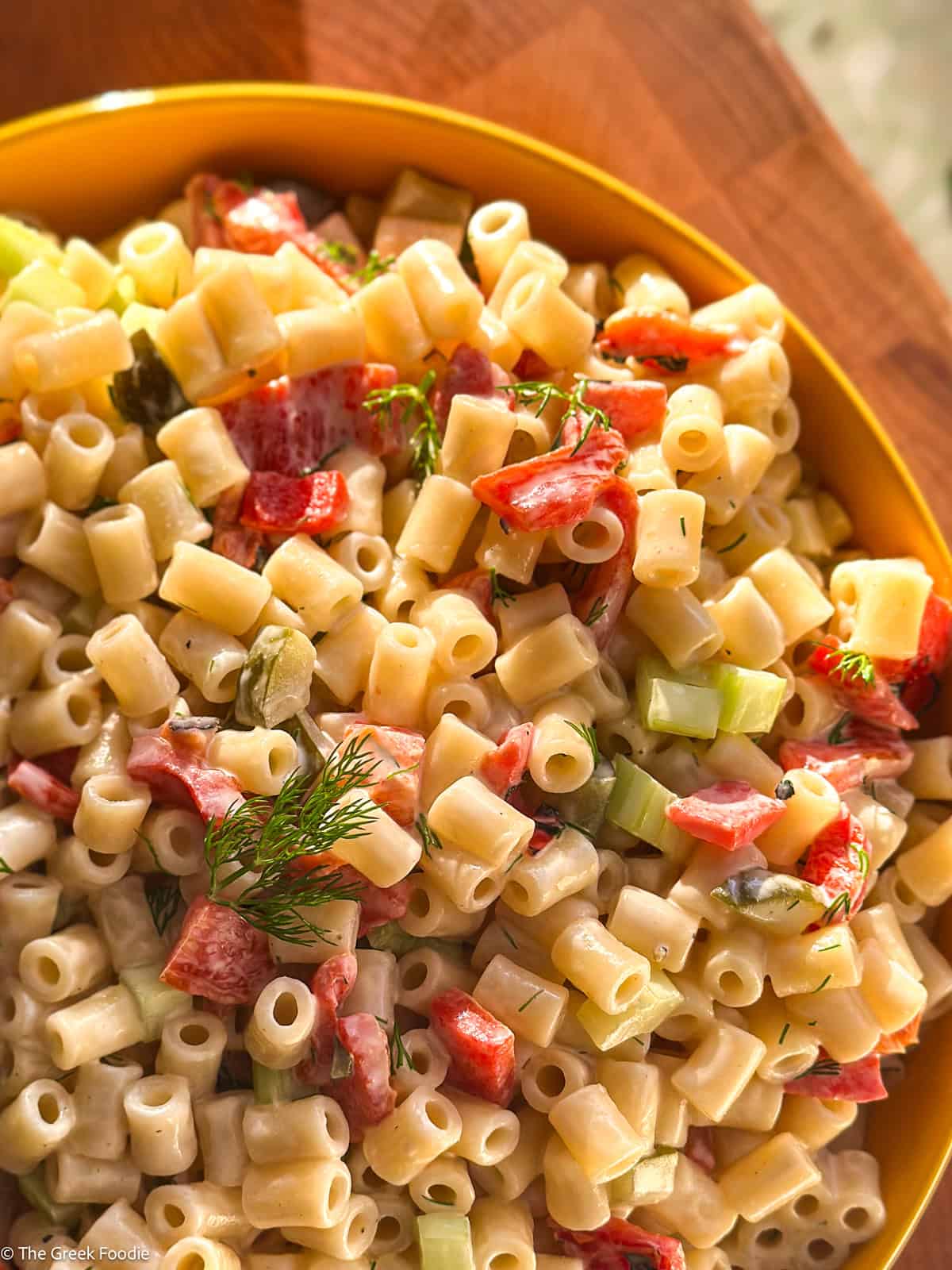 Close-up of creamy ditalini pasta salad with dill pickles, roasted red peppers, celery and sprigs of fresh dill.