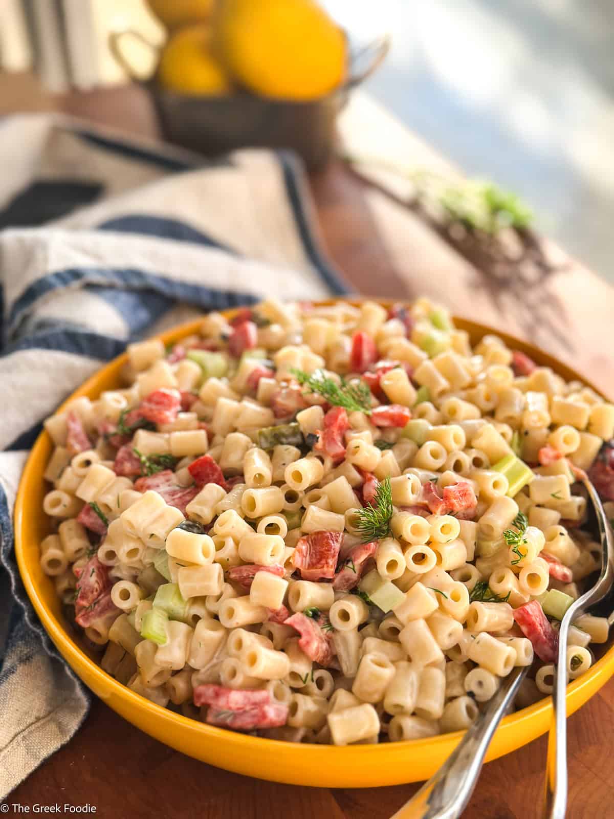Creamy dill pickle pasta salad with celery and roasted red peppers in a yellow bowl, served with two spoons.