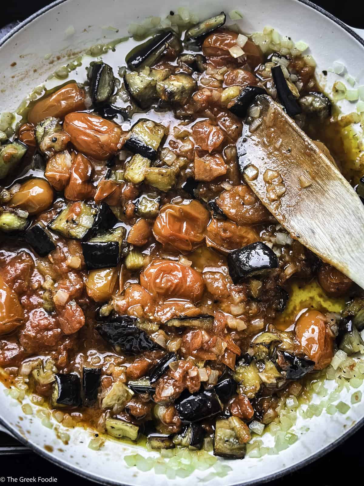Diced roasted eggplants and roasted tomatoes cooking in a white pot.