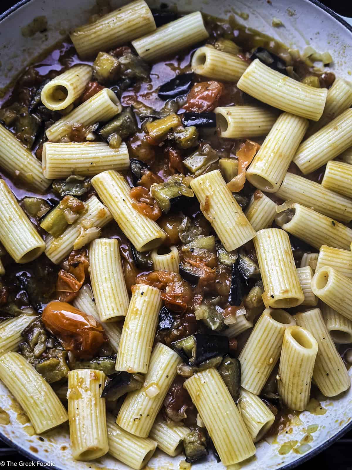 Pasta, roasted eggplants and roasted tomatoes cooking in a white pot.