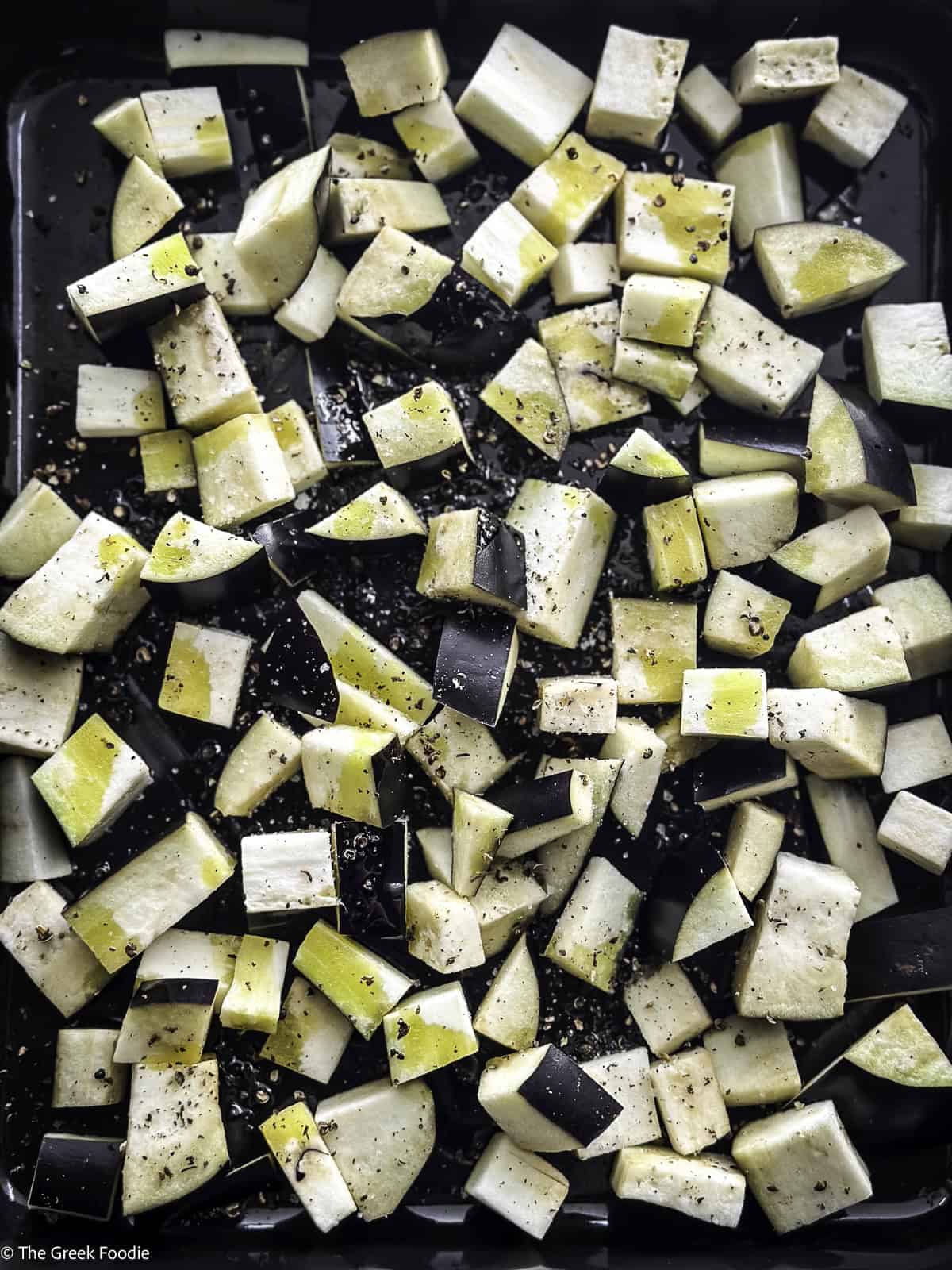 Eggplant cubes dressed with olive oil and seasonings in a roasting pan.