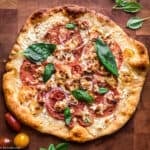 A feta pizza on a cutting board and basil leaves scattered on top.