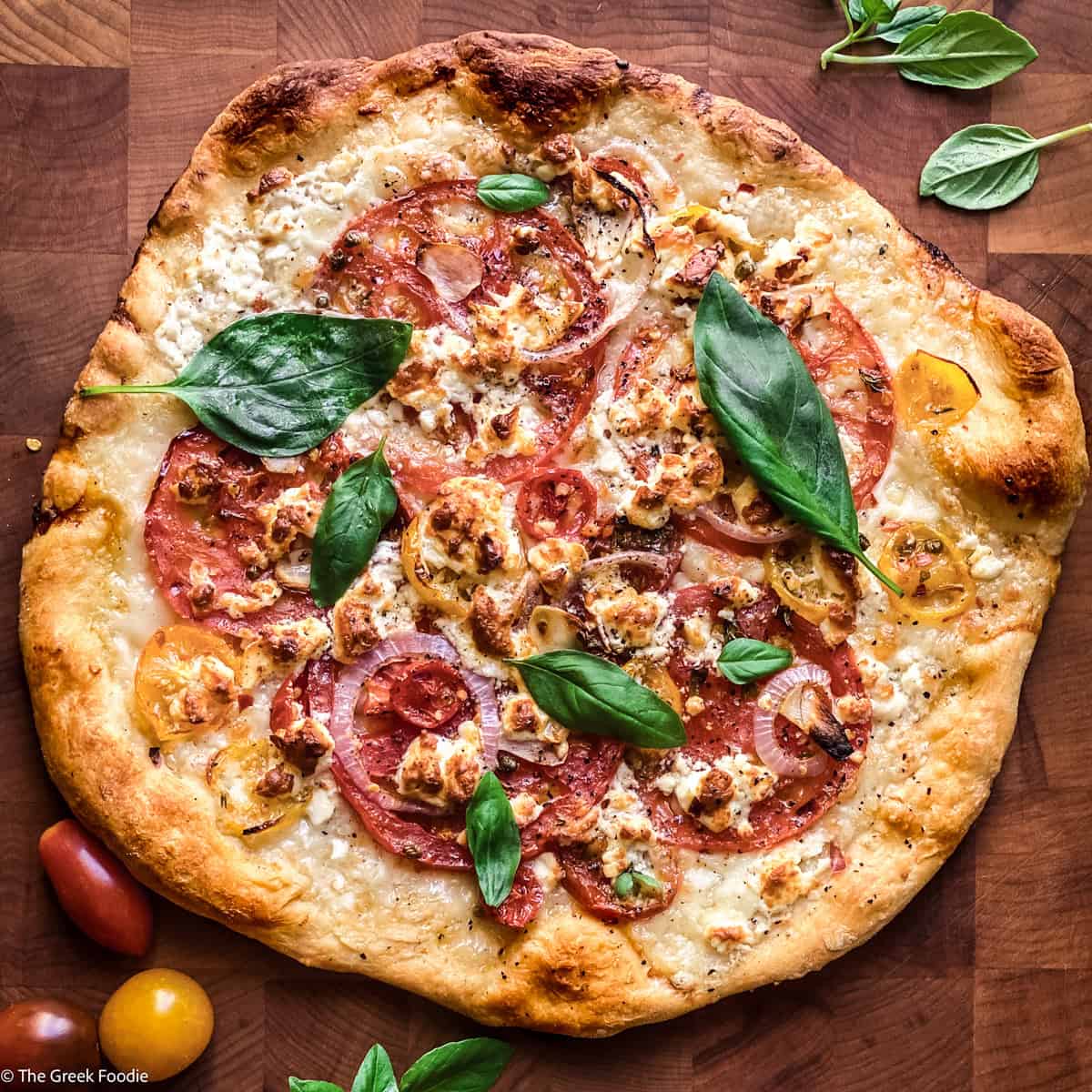 A feta pizza on a cutting board and basil leaves scattered on top.