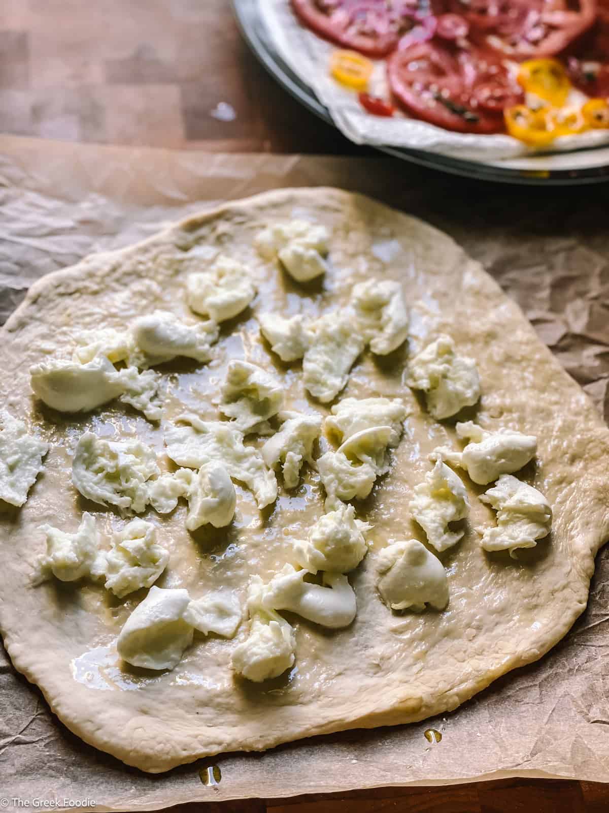 Pizza dough on parchment paper with shredded mozzarella on top.