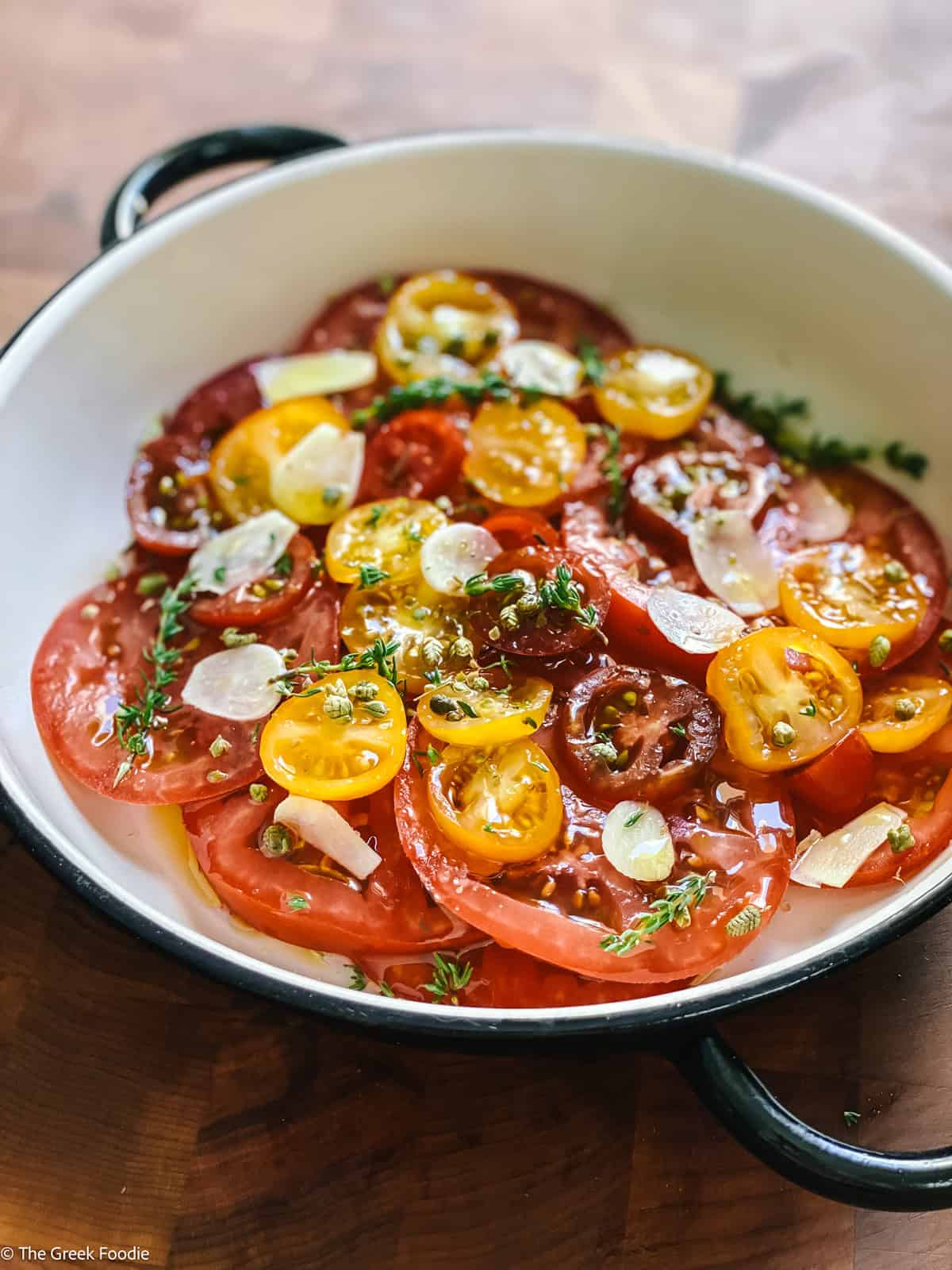 Sliced tomatoes in a shallow bowl with herbs and olive oil.