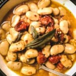 Gigantes beans with roasted tomatoes, two sage leaves in a bowl and a spoon.