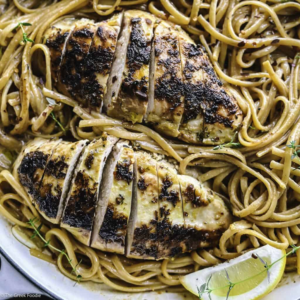 A plate with lemon chicken pasta an a lemon wedge.