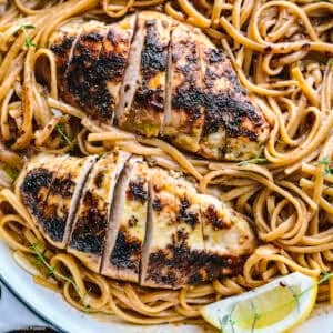 A plate with lemon chicken pasta an a lemon wedge.