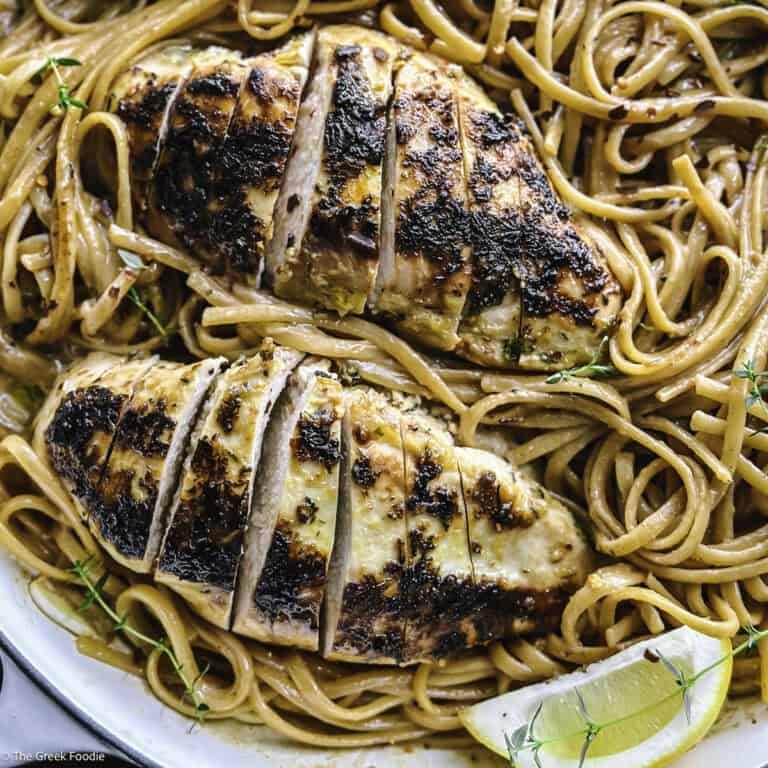 A plate with lemon chicken pasta an a lemon wedge.