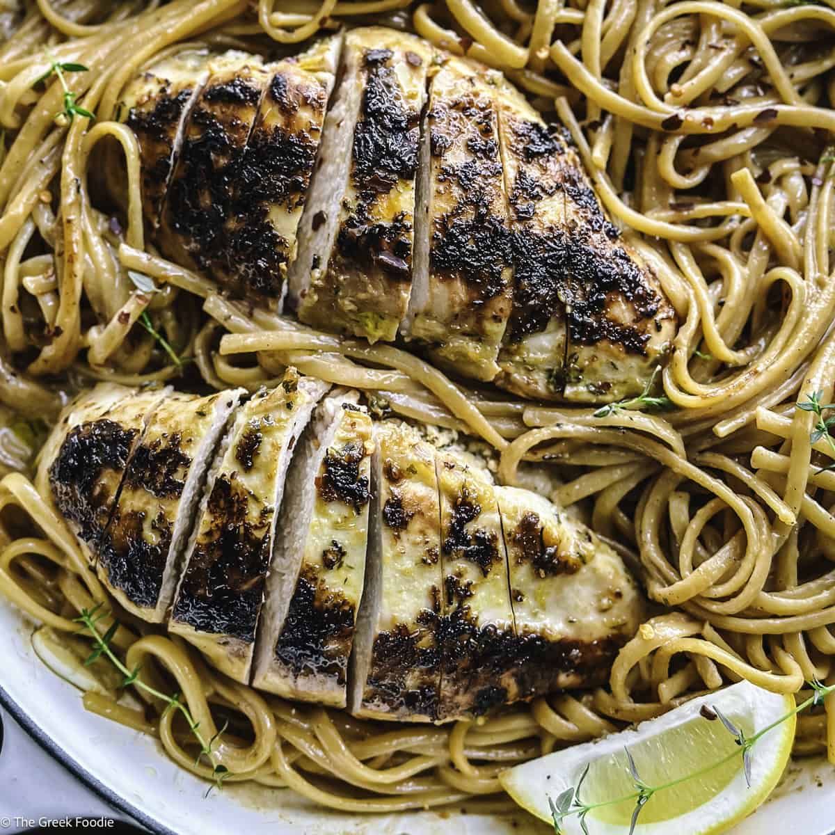 A plate with lemon chicken pasta an a lemon wedge.