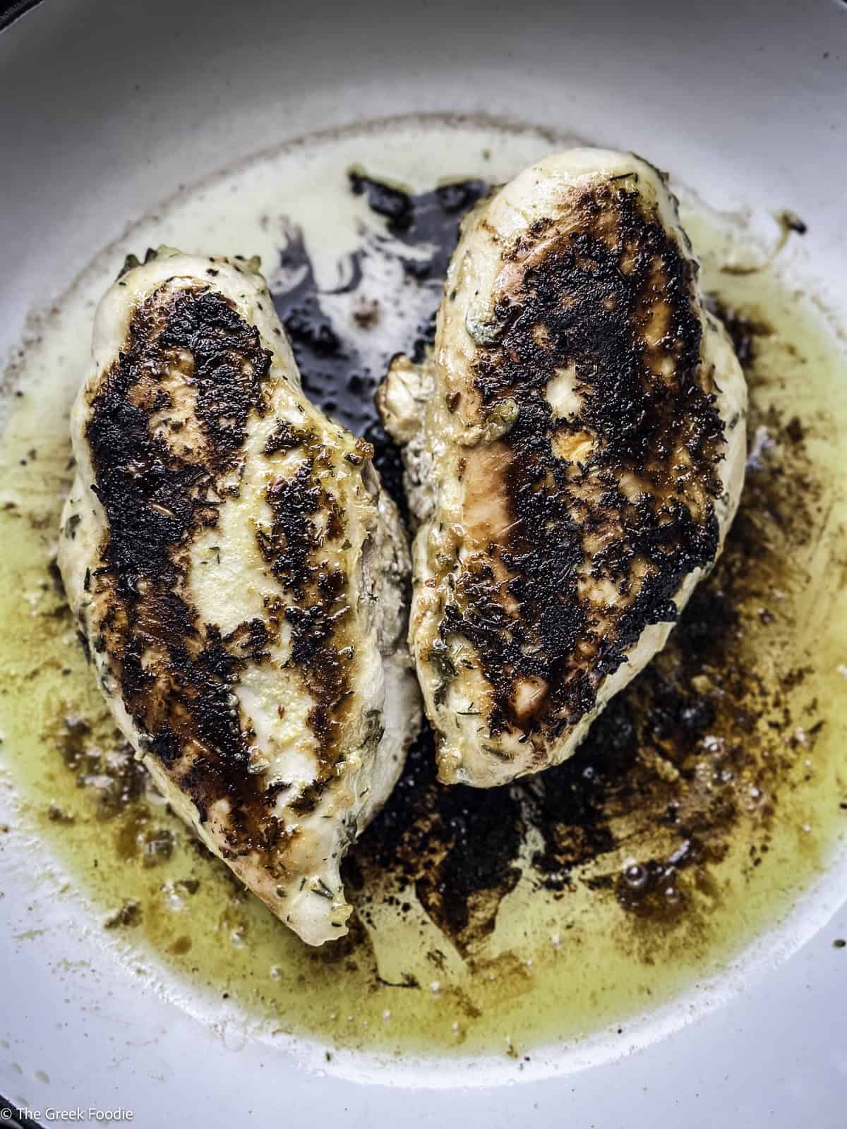 Two chicken breasts cooking in a skillet.