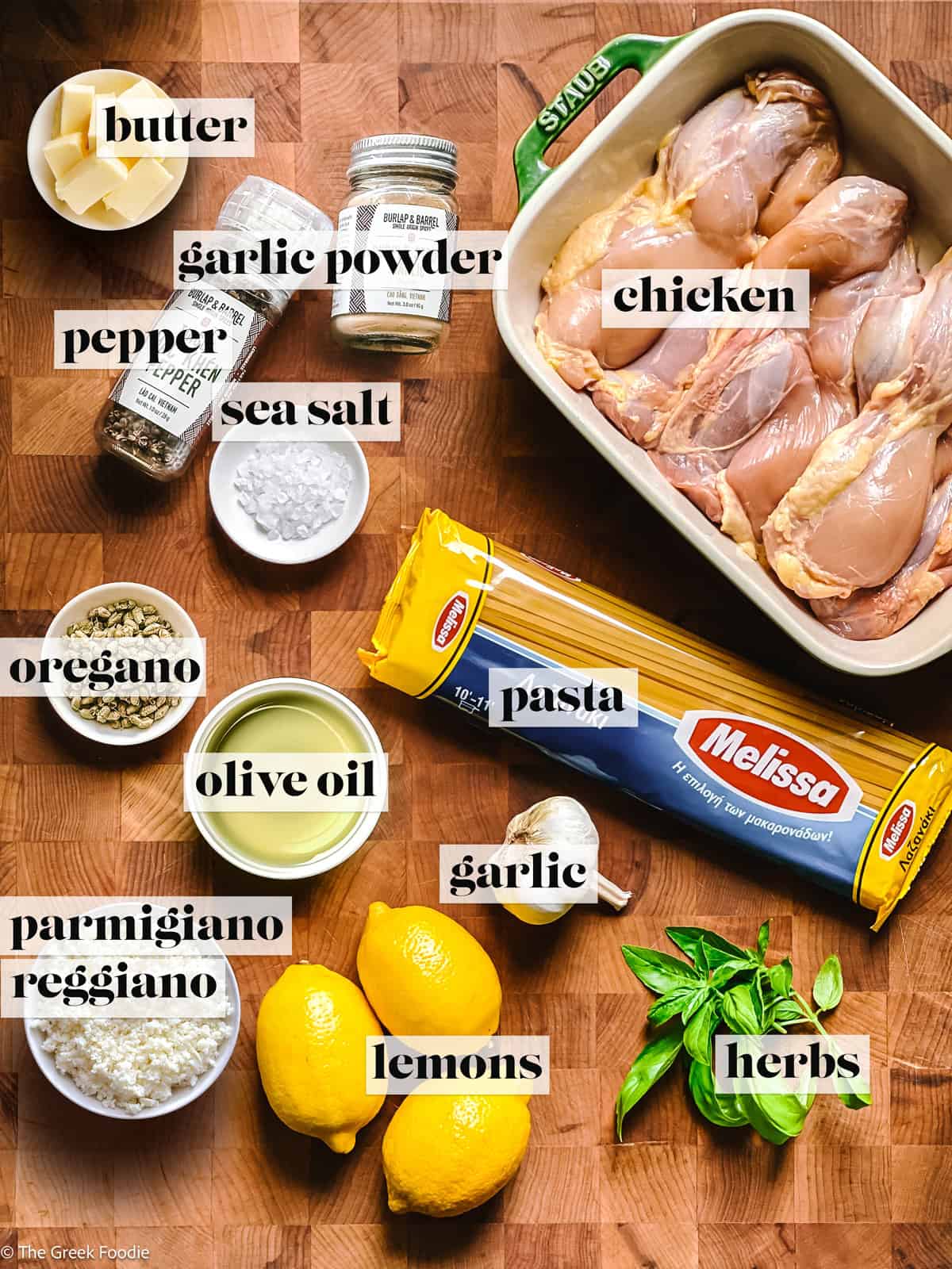 Chicken, lemons, butter and olive oil, pasta, garlic and seasonings on a wooden surface, overheard view.