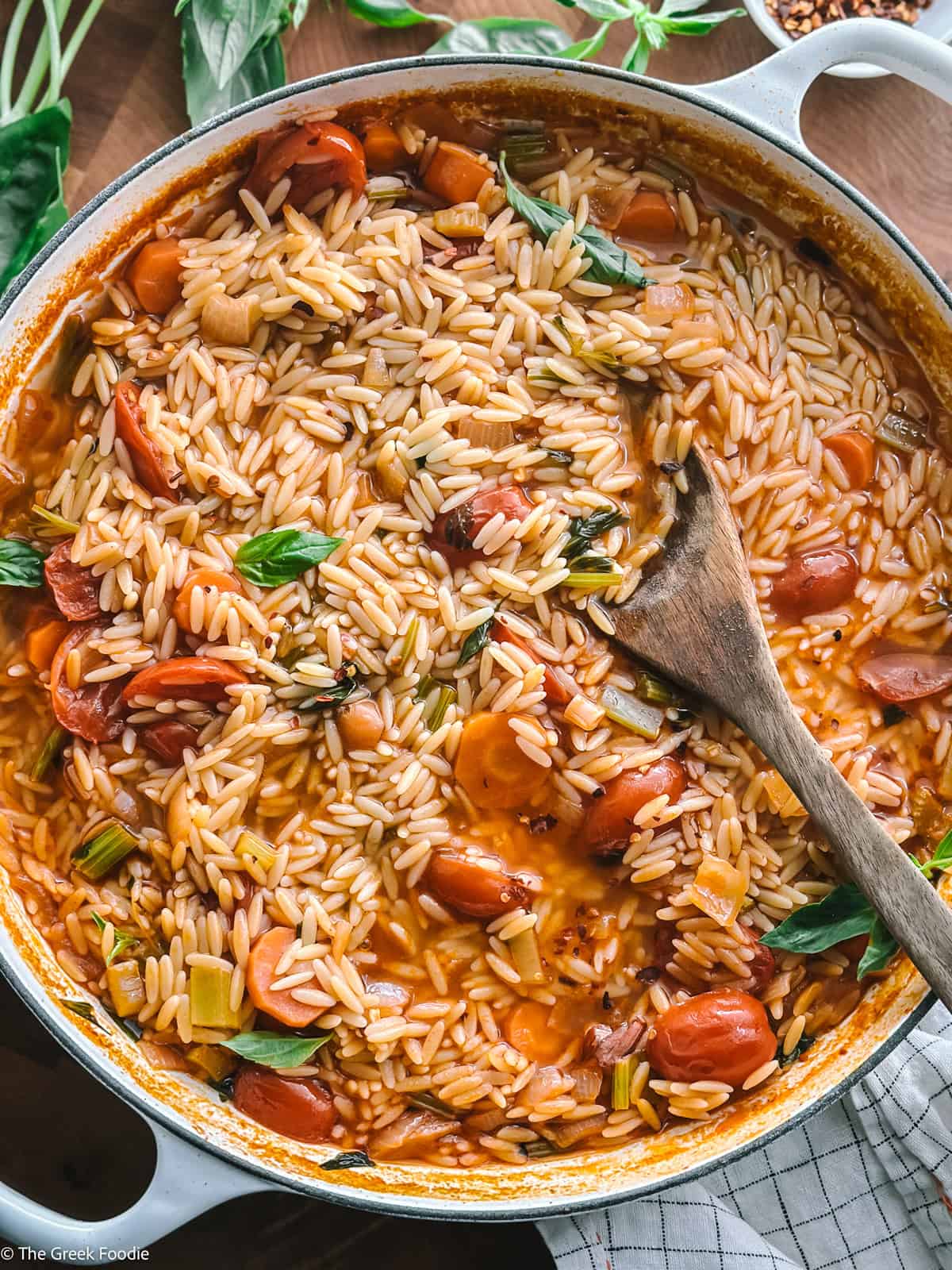A pot with manestra-Greek orzo soup, on a table with a wooden spoon.