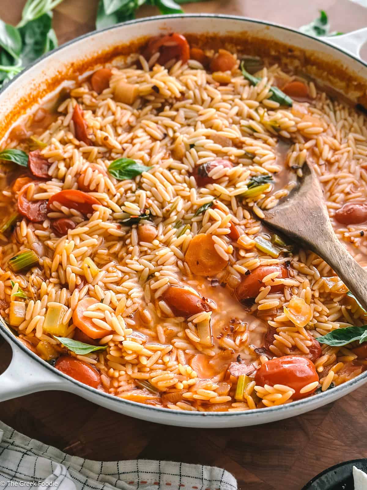 A pot with manestra-Greek orzo soup, on a table with a wooden spoon.