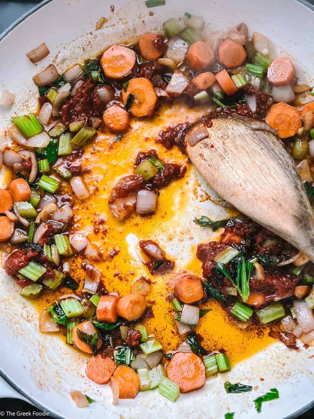 Vegetables, tomato paste and seasoning in a pot with a wooden spoon.