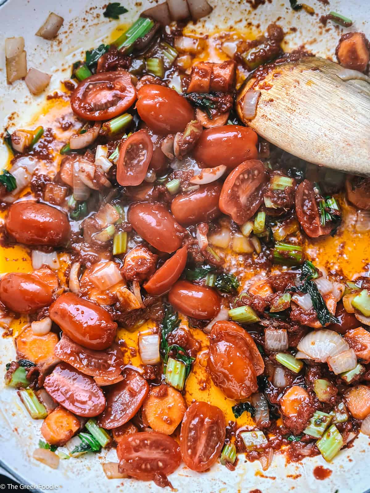 Vegetables and seasoning in a pot with a wooden spoon.
