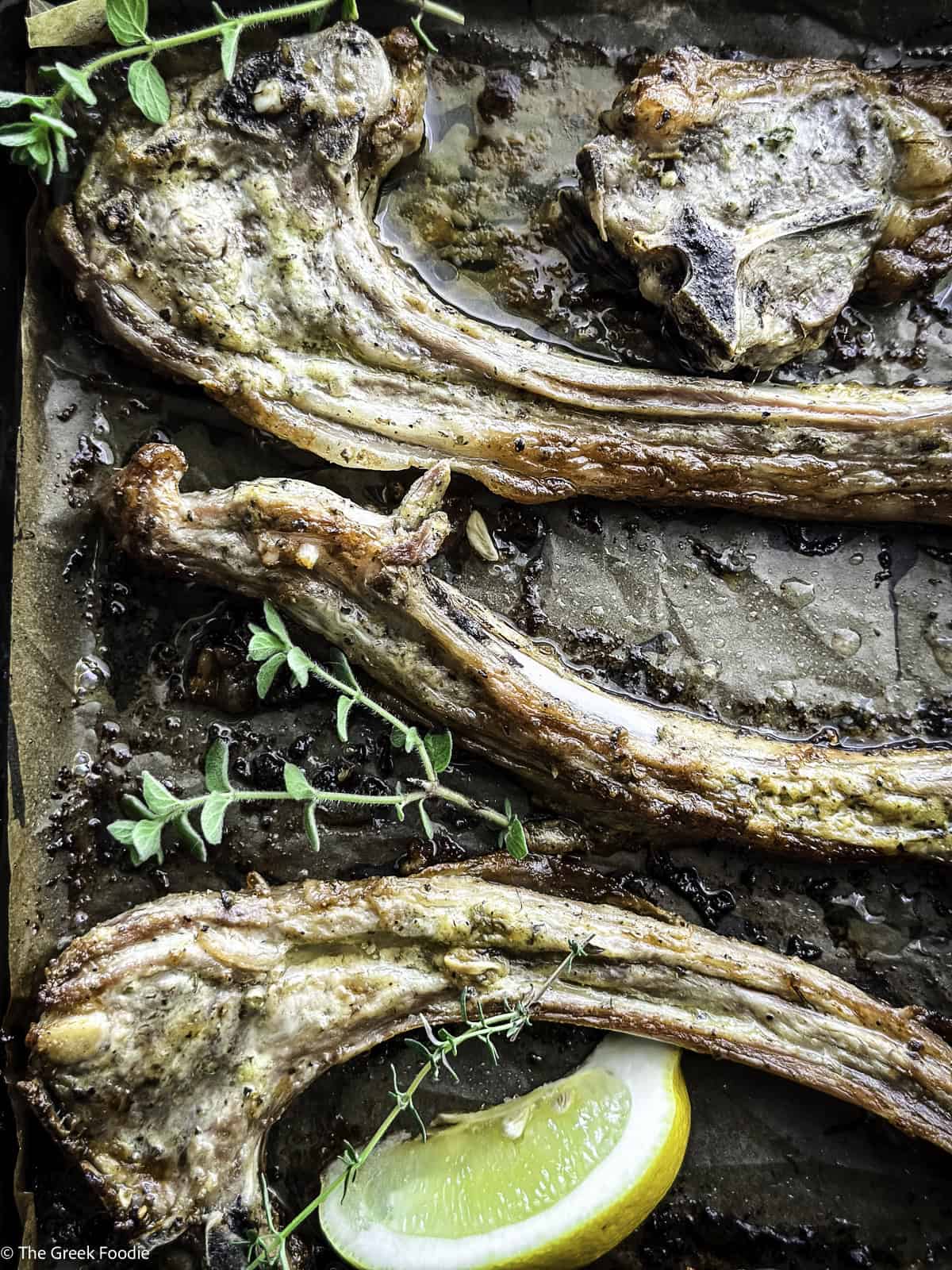 Close up of Greek lamb chops paidakia on parchment paper with a slice of lemon and fresh thyme.