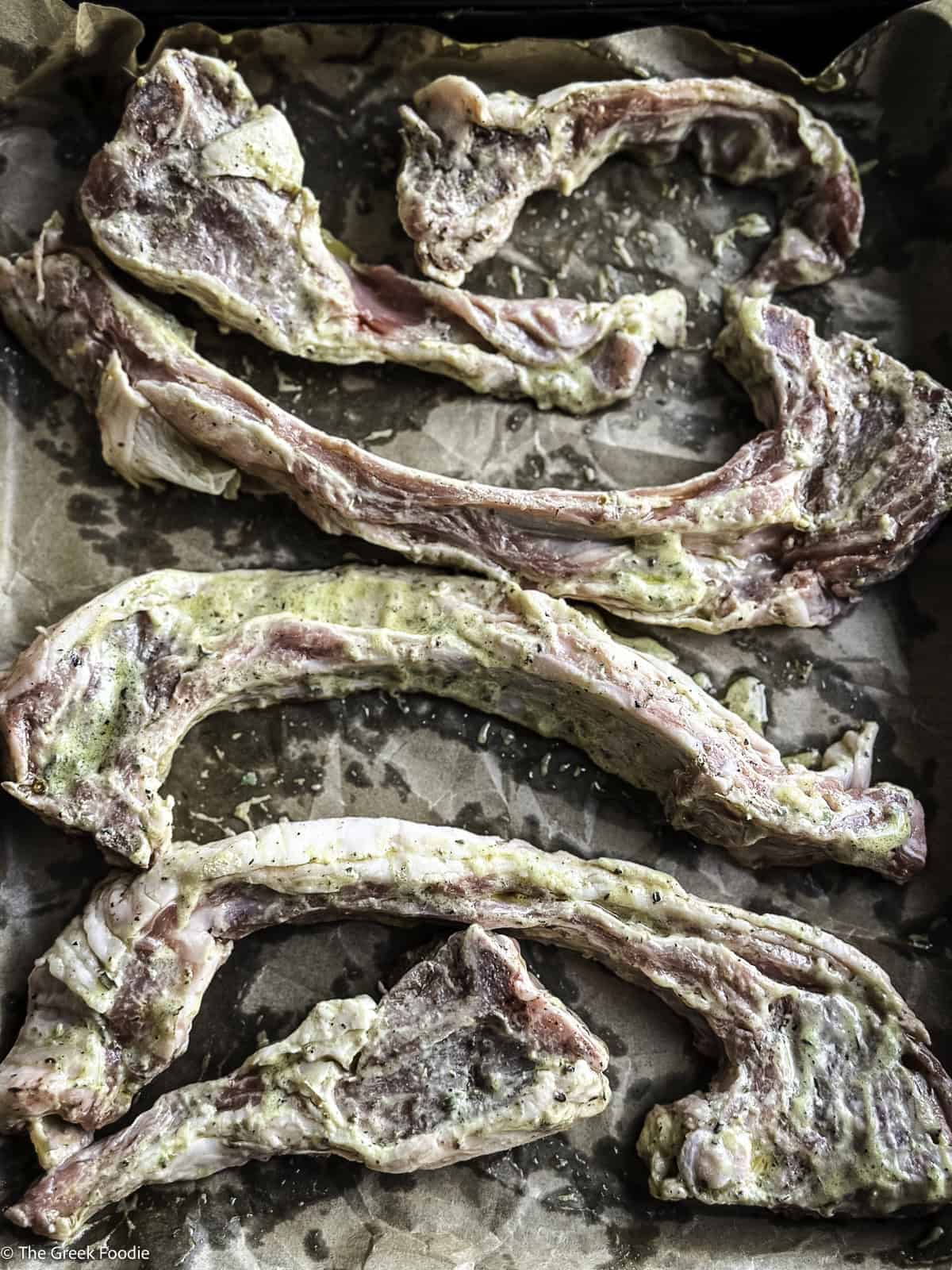 Close up of Greek lamb chops paidakia on parchment paper with marinade.