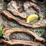 Close up of Greek lamb chops paidakia on parchment paper with a slice of lemon and fresh thyme.