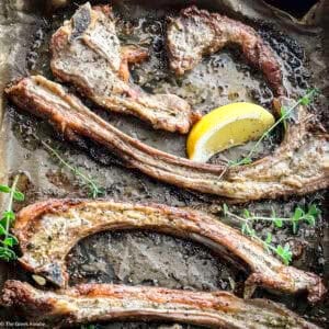 Close up of Greek lamb chops paidakia on parchment paper with a slice of lemon and fresh thyme.