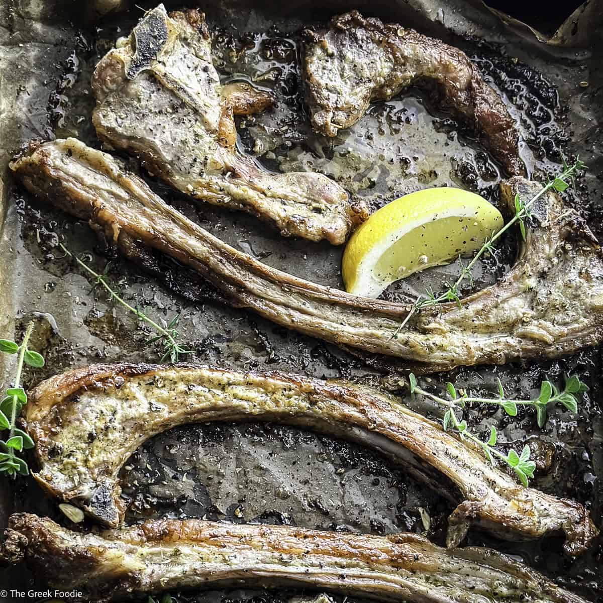 Close up of Greek lamb chops paidakia on parchment paper with a slice of lemon and fresh thyme.