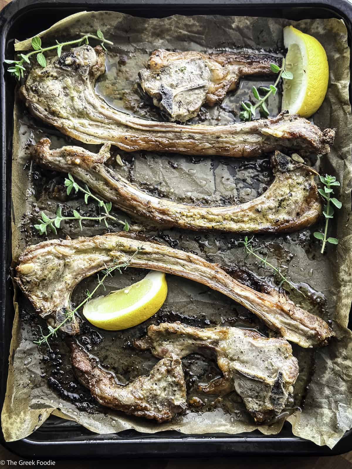 Close up of Greek lamb chops paidakia on parchment paper with a slice of lemon and fresh thyme.
