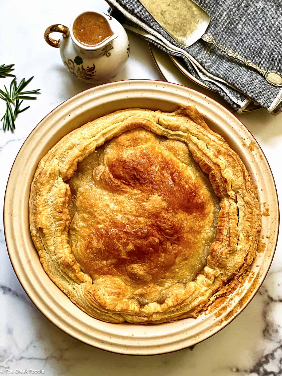 An apple pie in a round tart pan, a canister with sauce, naplins and serving utensils.