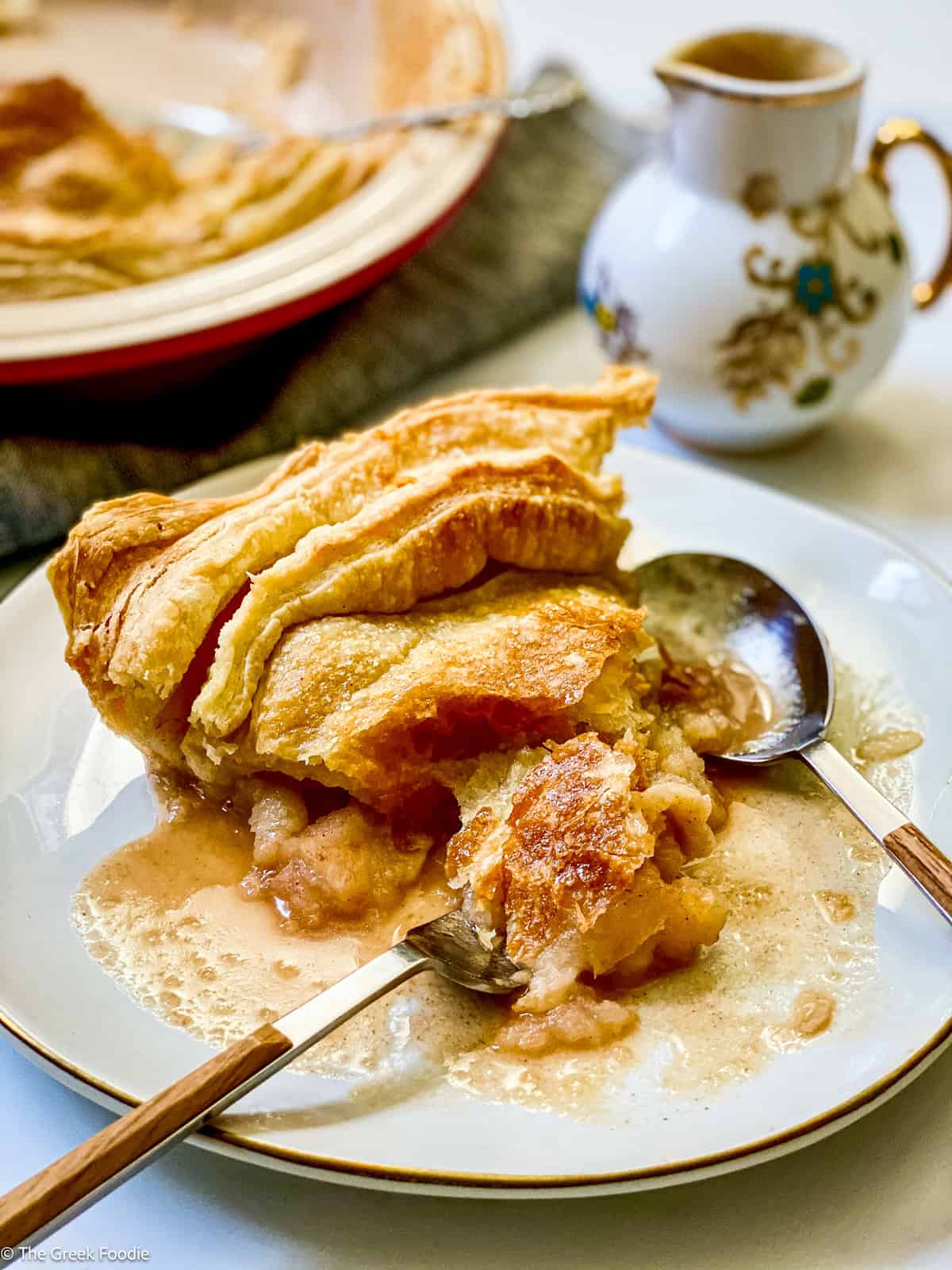 A piece of apple pie on a plate with a fork and spoon.