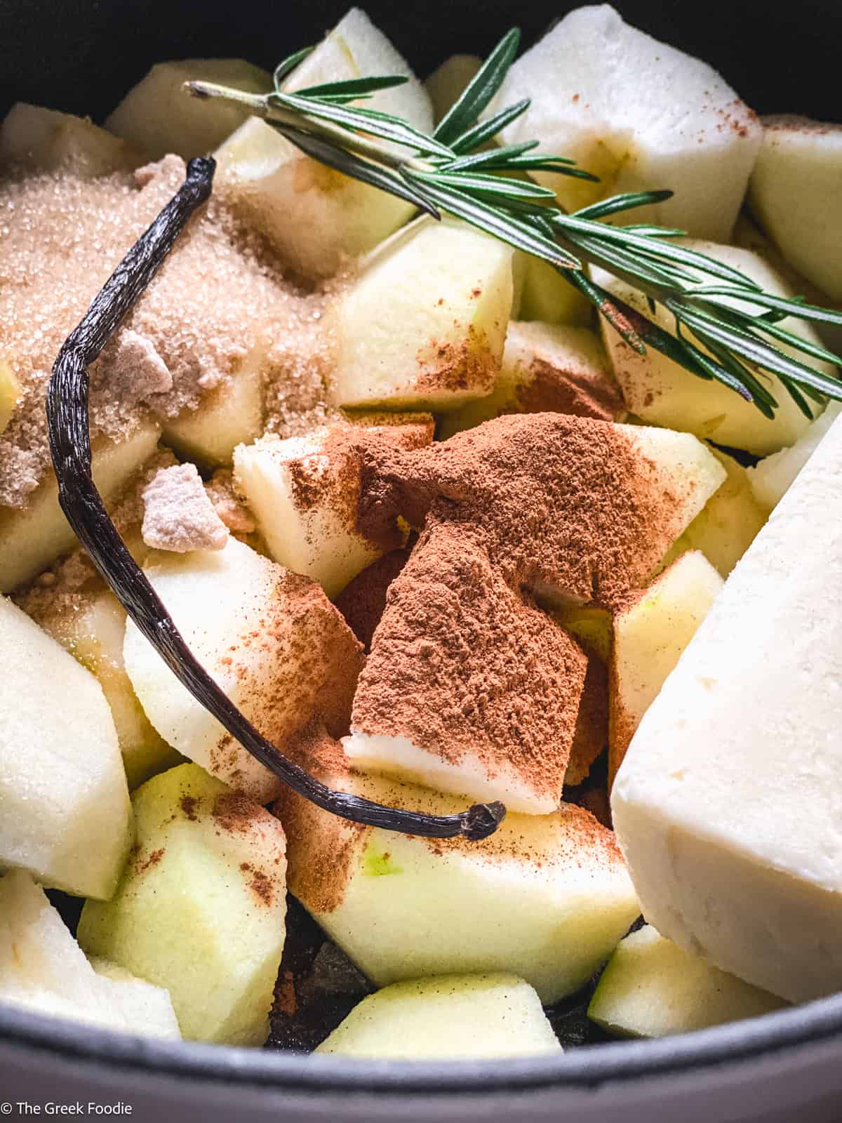 Apples, vanilla beans, rosemary and cinnamon is a saucepan.