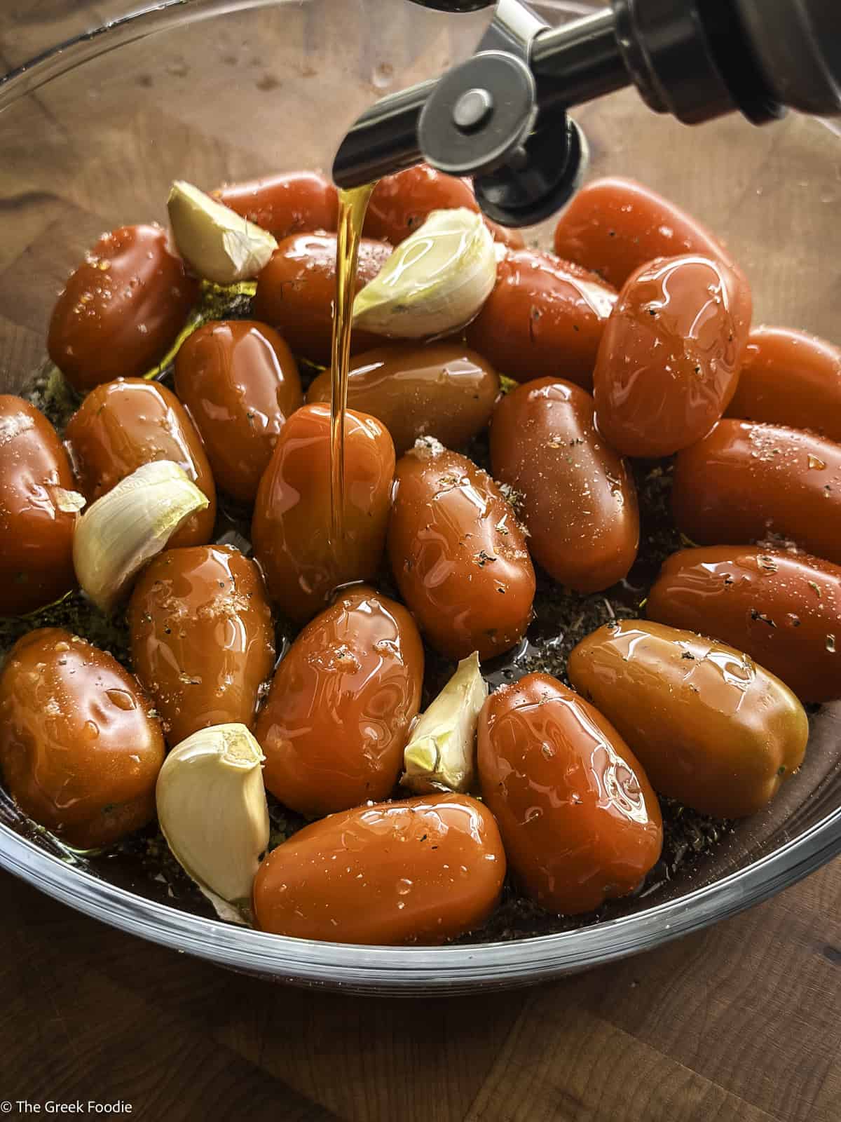 Cherry tomatoes and garlic cloves and a bottle pouring olive oil.