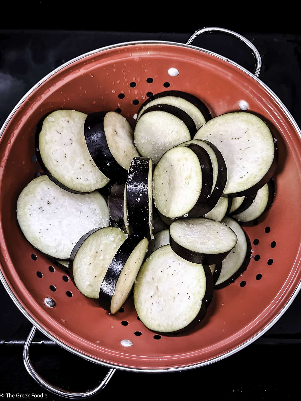 Eggplant slices in a red colander.