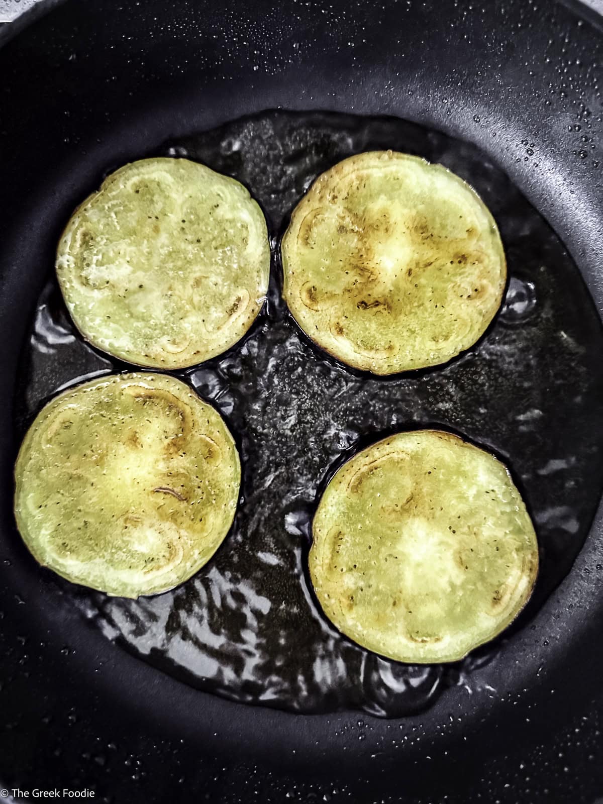 Four eggplant slices frying.