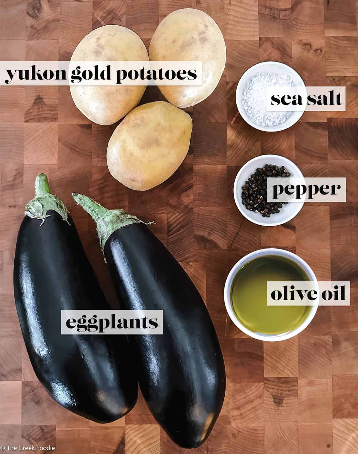 Eggplants, sea salt, pepper and potatoes on a wooden surface.