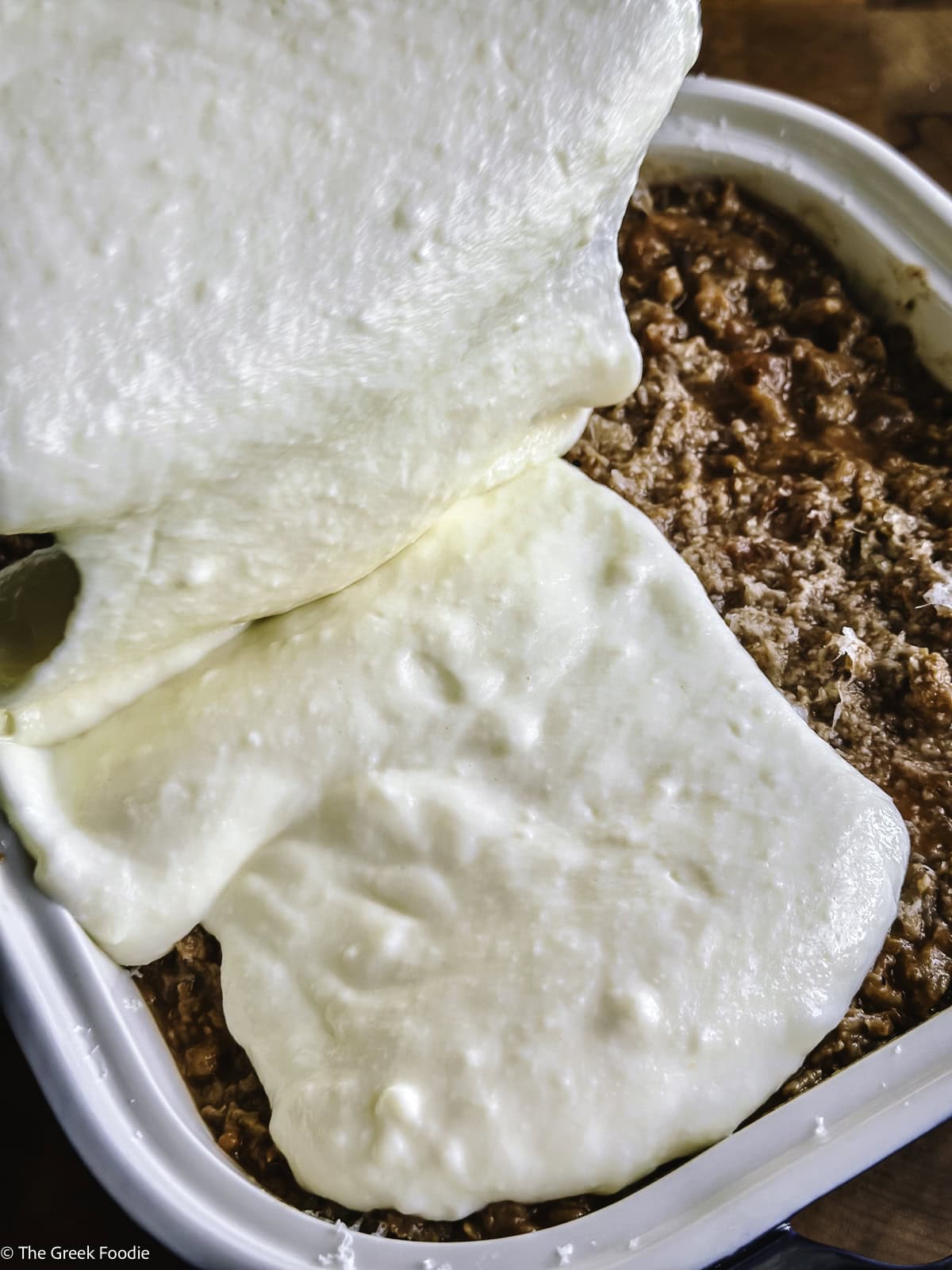 Bechamel sauce being poured over meat sauce.