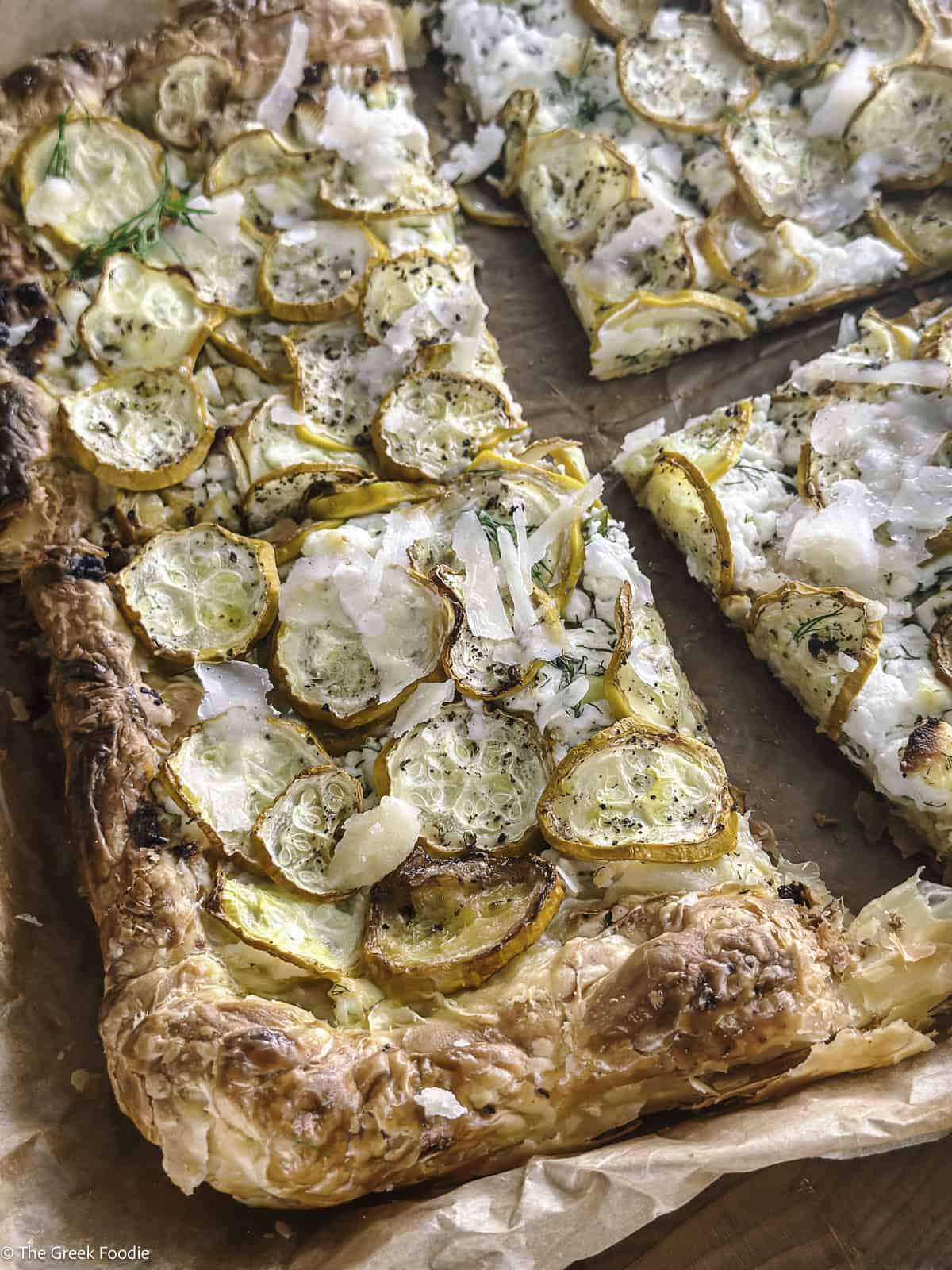A yellow zucchini puff pastry tart cut into four pieces on parchment paper.