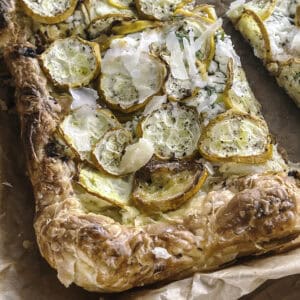A piece of zucchini puff pastry tart on parchment paper.