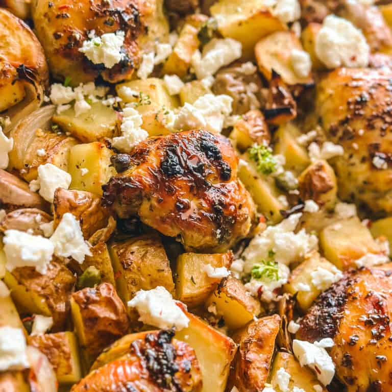 Close-up of roasted Greek chicken thighs with golden potatoes, olives, and feta