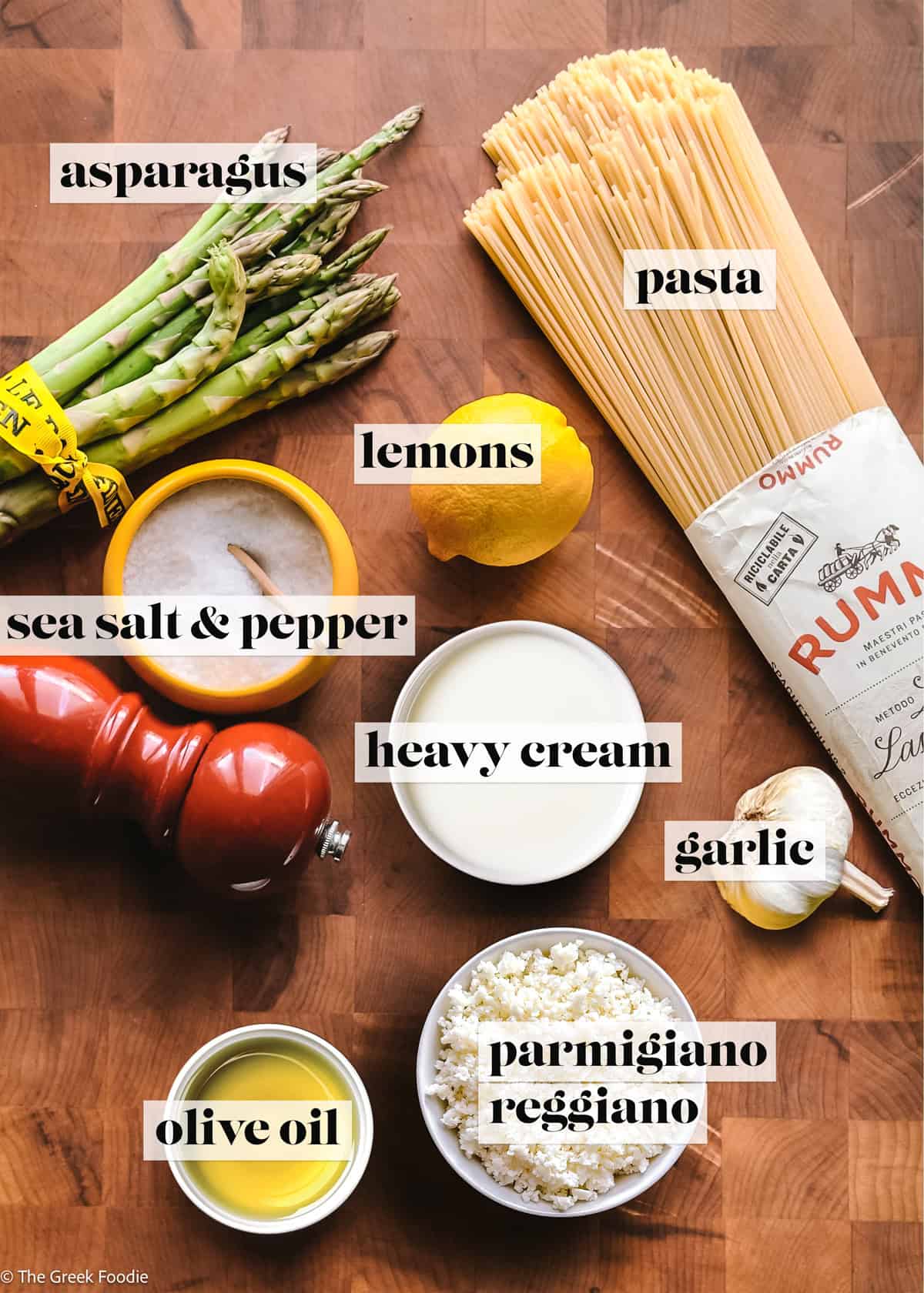 Asparagus, spaghetti, heavy cream, cheese olive oil, garlic, a lemon, sea salt and pepper on a table.