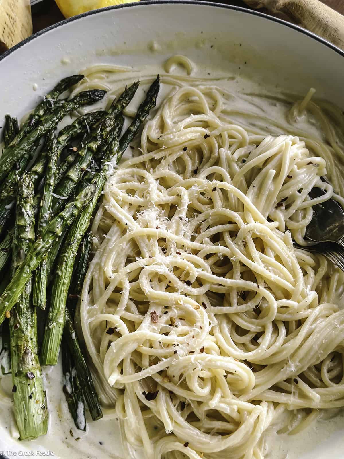 A plate with creamy asparagus pasta and utensils, and partial view of lemon, cheese and a wood juicer.