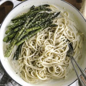 A plate with creamy asparagus pasta and utensils, and partial view of lemon, cheese and a wood juicer.