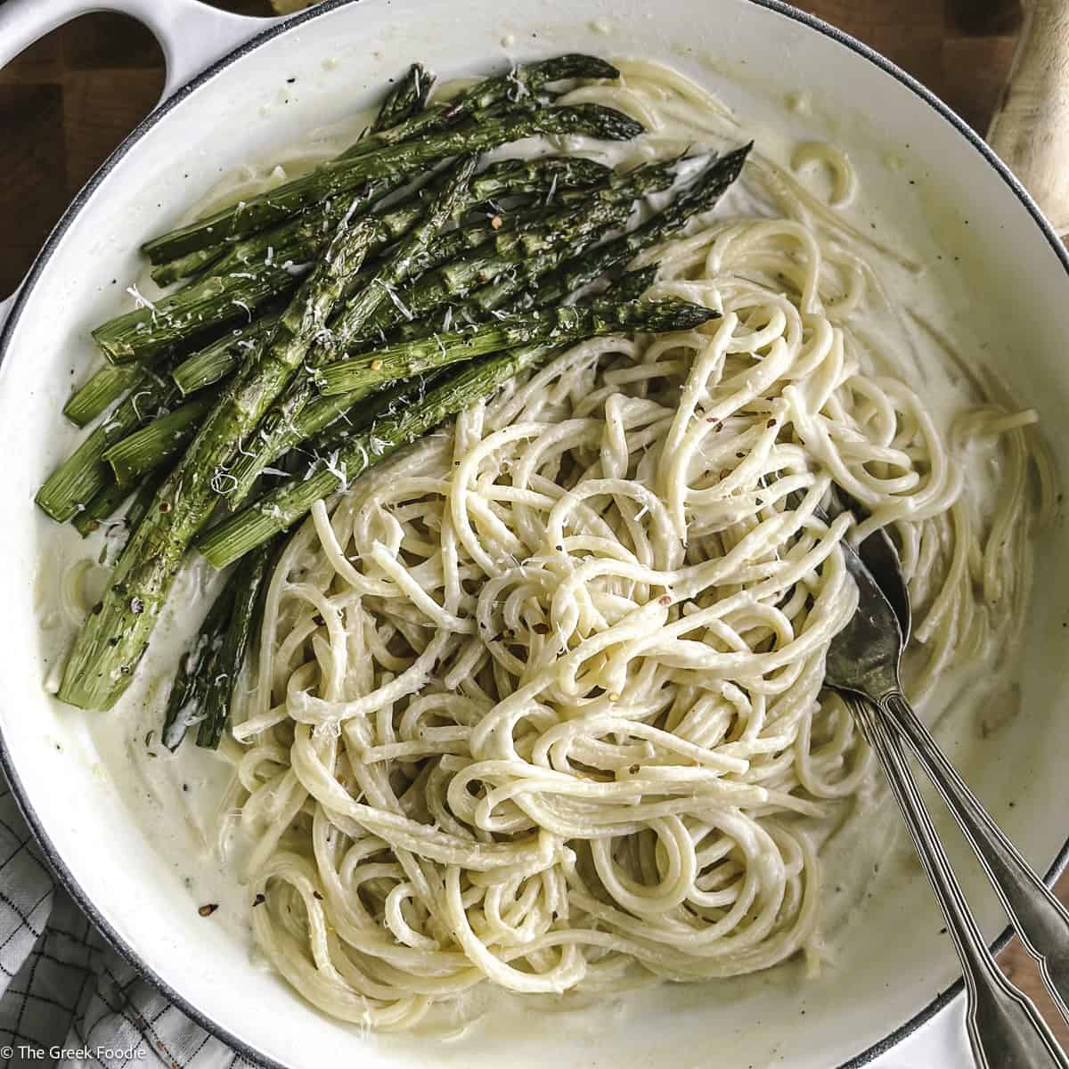 A plate with creamy asparagus pasta and utensils, and partial view of lemon, cheese and a wood juicer.
