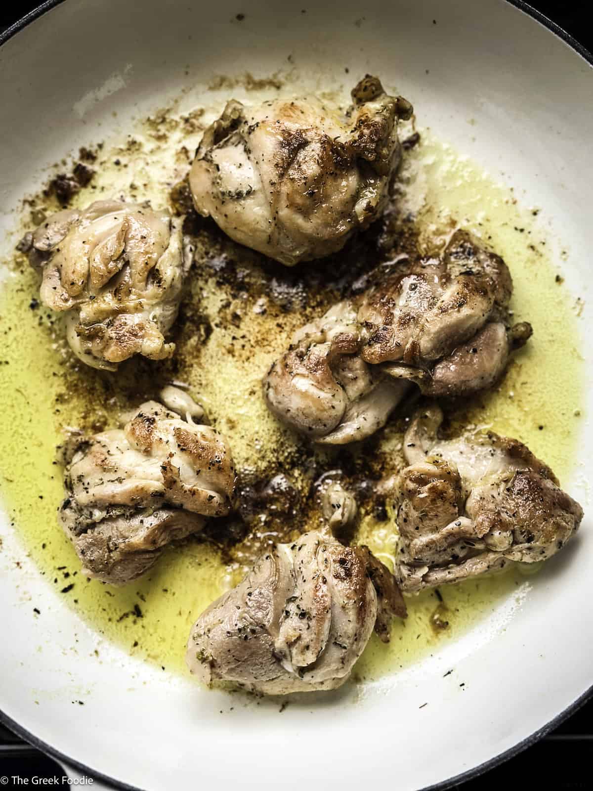 Chicken thighs cooking in a white skillet.